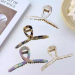 A gold-toned metal hair claw clip with a sleek, rainbow marble pattern on the top panel. By Clothifydotpk