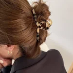 A gold-toned metal hair claw clip with a sleek, leopard print marble pattern on the top panel. By Clothifydotpk
