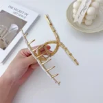 A gold-toned metal hair claw clip with a sleek, rainbow marble pattern on the top panel. By Clothifydotpk