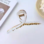 A gold-toned metal hair claw clip with a sleek, white marble pattern on the top panel. By Clothifydotpk