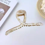 A gold-toned metal hair claw clip with a sleek, pearl white marble pattern on the top panel. By Clothifydotpk