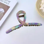 A gold-toned metal hair claw clip with a sleek, rainbow marble pattern on the top panel. By Clothifydotpk