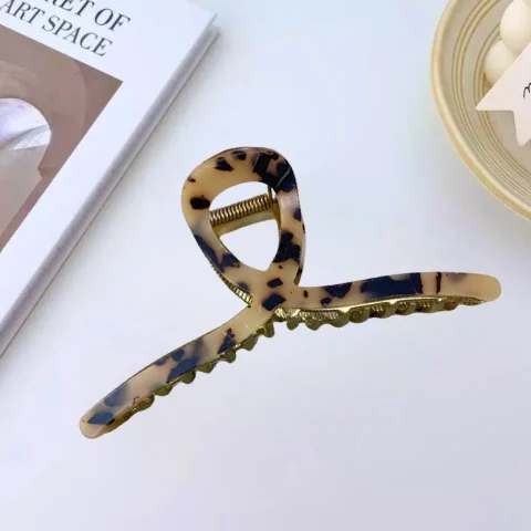 A gold-toned metal hair claw clip with a sleek, leopard print marble pattern on the top panel. By Clothifydotpk
