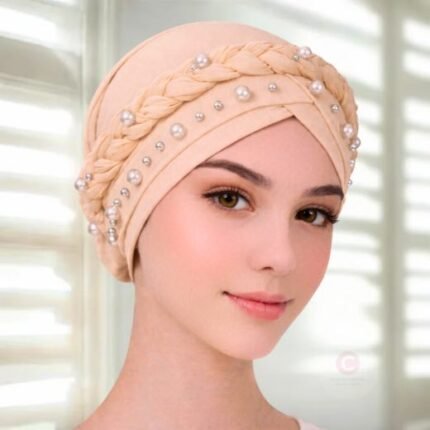 A woman wearing a fancy pearl turban hijab cap with delicate pearls, visible under a sheer or light hijab.