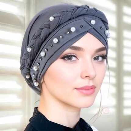 A woman wearing a fancy pearl turban hijab cap with delicate pearls, visible under a sheer or light hijab.