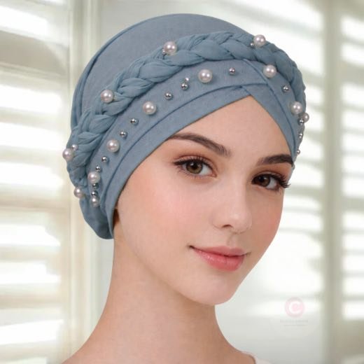 A woman wearing a fancy pearl turban hijab cap with delicate pearls, visible under a sheer or light hijab.