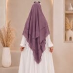 A woman wearing a three layer khimar hijab, with the first layer covering her head and draping down over her chest, and two additional sheer or lightweight layers cascading underneath. BY CLOTHIFYDOTPK