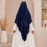 A woman wearing a three layer khimar, with the first layer covering her head and draping down over her chest, and two additional sheer or lightweight layers cascading underneath. BY CLOTHIFYDOTPK