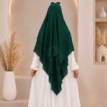 A woman wearing a three layer khimar hijab, with the first layer covering her head and draping down over her chest, and two additional sheer or lightweight layers cascading underneath. BY CLOTHIFYDOTPK