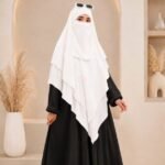 A woman wearing a white three layer khimar hijab, with the first layer covering her head and draping down over her chest, and two additional sheer or lightweight layers cascading underneath. BY CLOTHIFYDOTPK