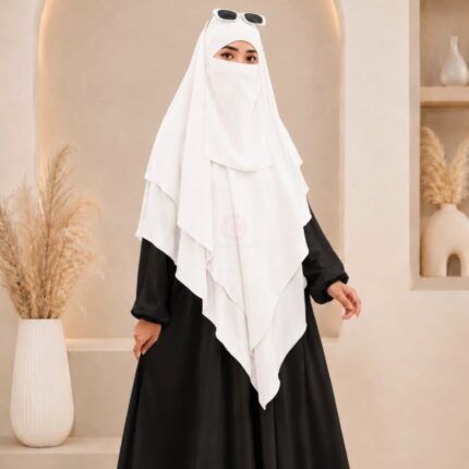 A woman wearing a white three layer khimar hijab, with the first layer covering her head and draping down over her chest, and two additional sheer or lightweight layers cascading underneath. BY CLOTHIFYDOTPK