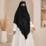 A woman wearing a three layer khimar, with the first layer covering her head and draping down over her chest, and two additional sheer or lightweight layers cascading underneath. BY CLOTHIFYDOTPK
