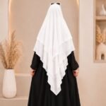 A woman wearing a white three layer khimar hijab, with the first layer covering her head and draping down over her chest, and two additional sheer or lightweight layers cascading underneath. BY CLOTHIFYDOTPK