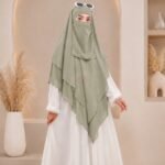 A woman wearing a white 3 layer khimar hijab, with the first layer covering her head and draping down over her chest, and two additional sheer or lightweight layers cascading underneath. BY CLOTHIFYDOTPK