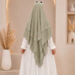 A woman wearing a white 3 layer khimar hijab, with the first layer covering her head and draping down over her chest, and two additional sheer or lightweight layers cascading underneath. BY CLOTHIFYDOTPK