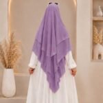 A woman wearing a three layer khimar, with the first layer covering her head and draping down over her chest, and two additional sheer or lightweight layers cascading underneath. BY CLOTHIFYDOTPK