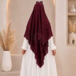 A woman wearing a three layer khimar, with the first layer covering her head and draping down over her chest, and two additional sheer or lightweight layers cascading underneath. BY CLOTHIFYDOTPK