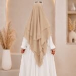 A woman wearing a three layer khimar hijab, with the first layer covering her head and draping down over her chest, and two additional sheer or lightweight layers cascading underneath. BY CLOTHIFYDOTPK