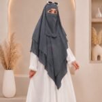 A woman wearing a three layer khimar hijab, with the first layer covering her head and draping down over her chest, and two additional sheer or lightweight layers cascading underneath. BY CLOTHIFYDOTPK