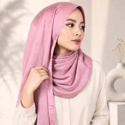Woman wearing an elegant stone silk hijab in a dusty rose color – soft fabric draping over her head and shoulder with natural lighting.