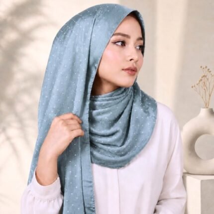 Woman wearing an elegant stone silk hijab in a ice blue color – soft fabric draping over her head and shoulder with natural lighting.