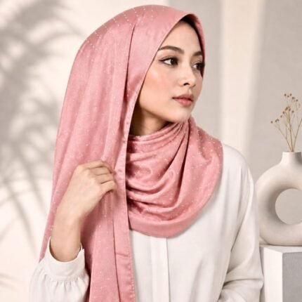 Woman wearing an elegant stone silk hijab in a peach color – soft fabric draping over her head and shoulder with natural lighting.