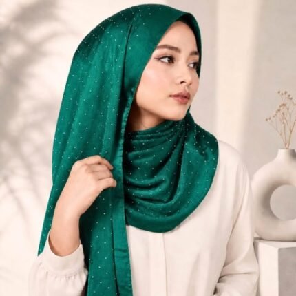 Woman wearing an elegant stone silk hijab in a peacock green color – soft fabric draping over her head and shoulder with natural lighting.