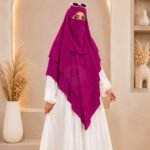 A woman wearing a three layer khimar hijab, with the first layer covering her head and draping down over her chest, and two additional sheer or lightweight layers cascading underneath. BY CLOTHIFYDOTPK