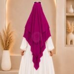 A woman wearing a three layer khimar hijab, with the first layer covering her head and draping down over her chest, and two additional sheer or lightweight layers cascading underneath. BY CLOTHIFYDOTPK