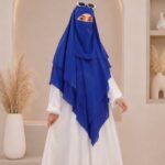 A woman wearing a three layer khimar, with the first layer covering her head and draping down over her chest, and two additional sheer or lightweight layers cascading underneath. BY CLOTHIFYDOTPK