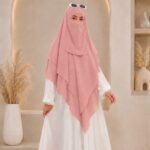 A woman wearing a three layer khimar with niqab , the first layer covering her head and draping down over her chest, and two additional sheer or lightweight layers cascading underneath. BY CLOTHIFYDOTPK