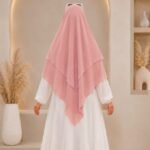 A woman wearing a three layer khimar with niqab , the first layer covering her head and draping down over her chest, and two additional sheer or lightweight layers cascading underneath. BY CLOTHIFYDOTPK