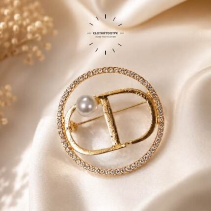 A close-up of a modern, sophisticated gold brooch featuring a brilliant arrangement of a pearl and clear rhinestones that catch the light. By Clothifydotpk