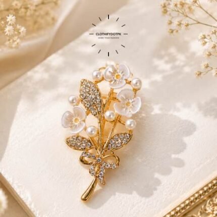 A close-up of a modern, sophisticated brooch featuring a brilliant arrangement of clear rhinestones and pearls that catch the light. By Clothifydotpk