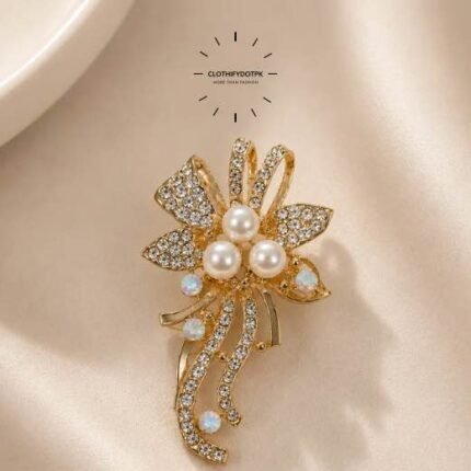 A close-up of a modern, sophisticated brooch featuring a brilliant arrangement of clear rhinestones and pearls that catch the light. By Clothifydotpk