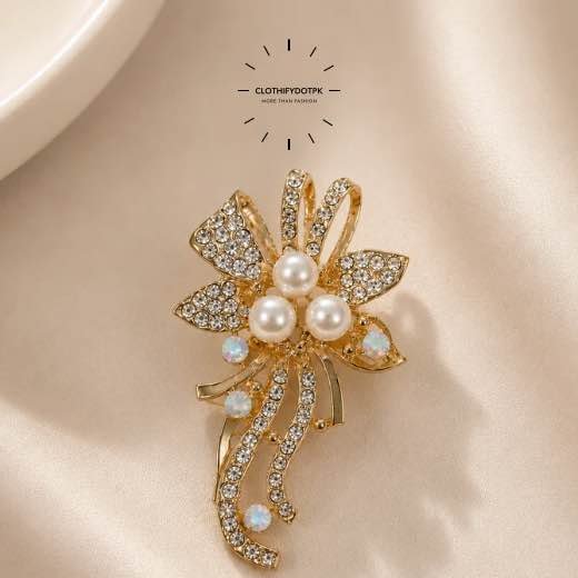 A close-up of a modern, sophisticated brooch featuring a brilliant arrangement of clear rhinestones and pearls that catch the light. By Clothifydotpk