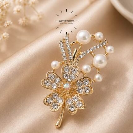 A close-up of a modern, sophisticated brooch featuring a brilliant arrangement of clear rhinestones and pearls that catch the light. By Clothifydotpk