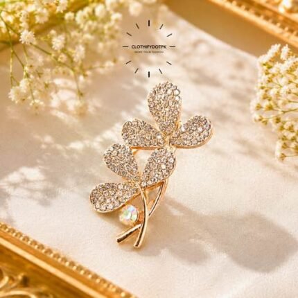 A close-up of a modern, sophisticated brooch featuring a brilliant arrangement of clear rhinestones and pearls that catch the light. By Clothifydotpk