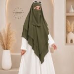 A woman wearing a three layer khimar, with the first layer covering her head and draping down over her chest, and two additional sheer or lightweight layers cascading underneath. BY CLOTHIFYDOTPK