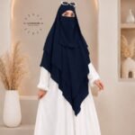 A woman wearing a three layer khimar, with the first layer covering her head and draping down over her chest, and two additional sheer or lightweight layers cascading underneath. BY CLOTHIFYDOTPK