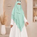A woman wearing a three layer khimar, with the first layer covering her head and draping down over her chest, and two additional sheer or lightweight layers cascading underneath. BY CLOTHIFYDOTPK