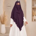 A woman wearing a three layer khimar hijab, with the first layer covering her head and draping down over her chest, and two additional sheer or lightweight layers cascading underneath. BY CLOTHIFYDOTPK