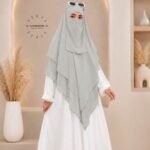 A woman wearing a three layer khimar, with the first layer covering her head and draping down over her chest, and two additional sheer or lightweight layers cascading underneath. BY CLOTHIFYDOTPK